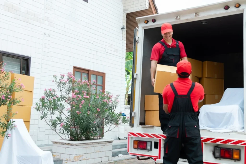 Two professional Melbourne movers working as a team — one on the moving truck receiving boxes and another standing below passing packed moving boxes during a house move